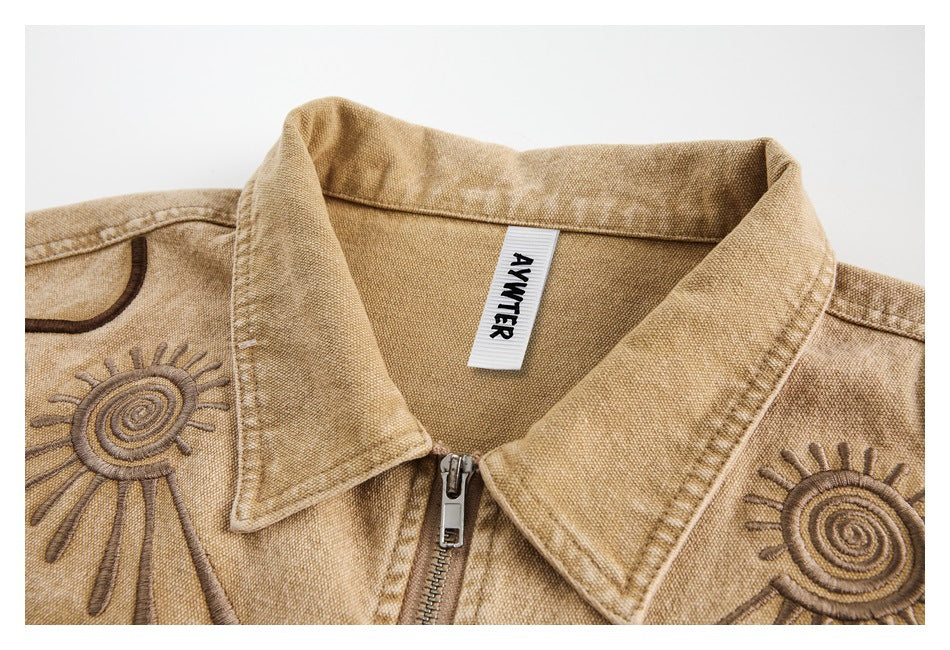 Close-up of the tan jacket's pointed collar, zipper, textured fabric, embroidered sun motifs, and neck label.