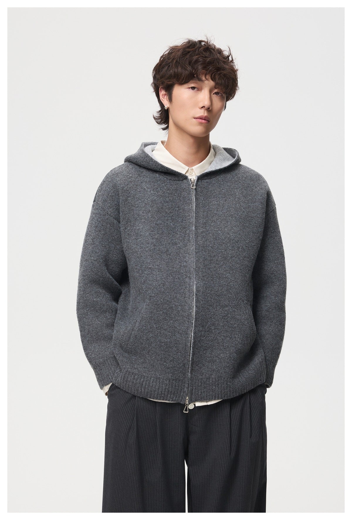 Model wearing a charcoal gray hooded zip cardigan over a white shirt and dark pinstripe trousers.