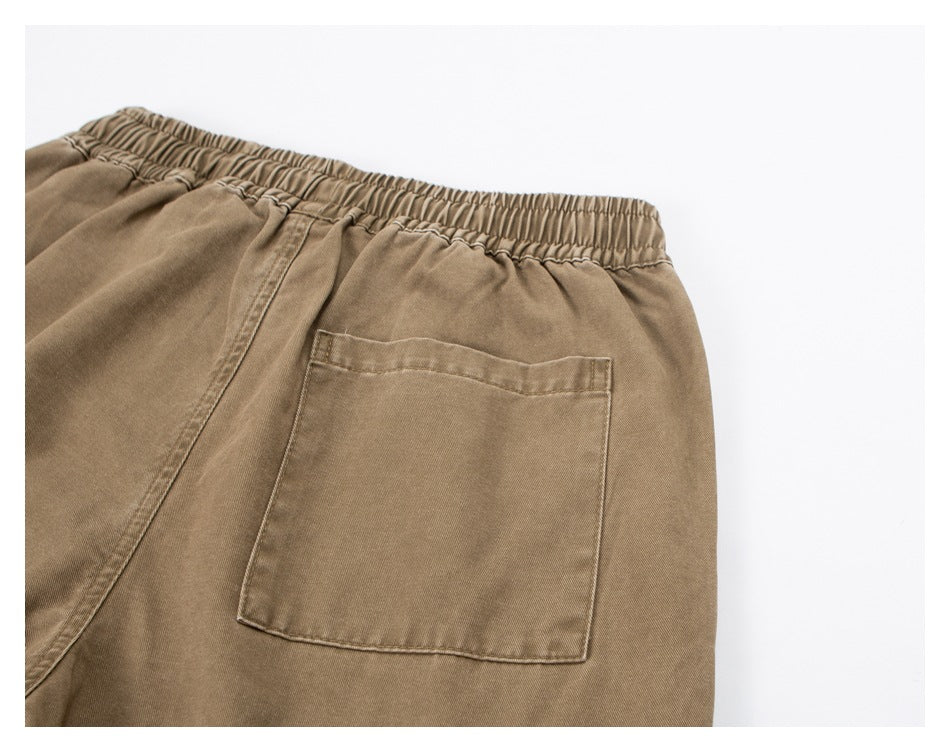 Close-up of tan trousers showing the gathered elastic waistband and a rectangular rear pocket.