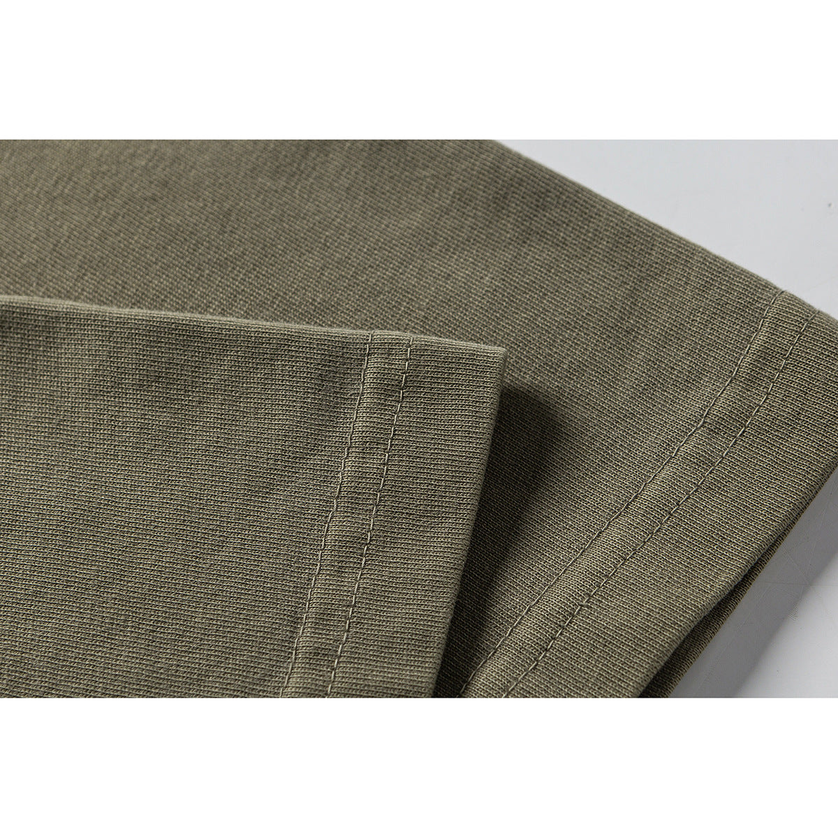 Close-up of olive-gray T-shirt fabric and double-stitched sleeve and hem edges.