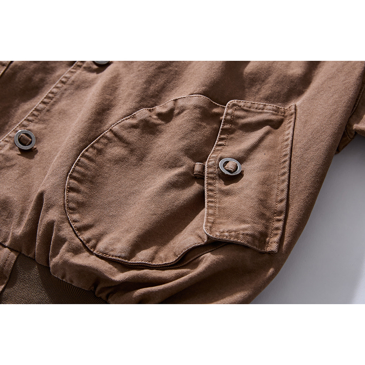Close-up of a brown jacket's large flap pocket and ring-style button, with visible stitching.