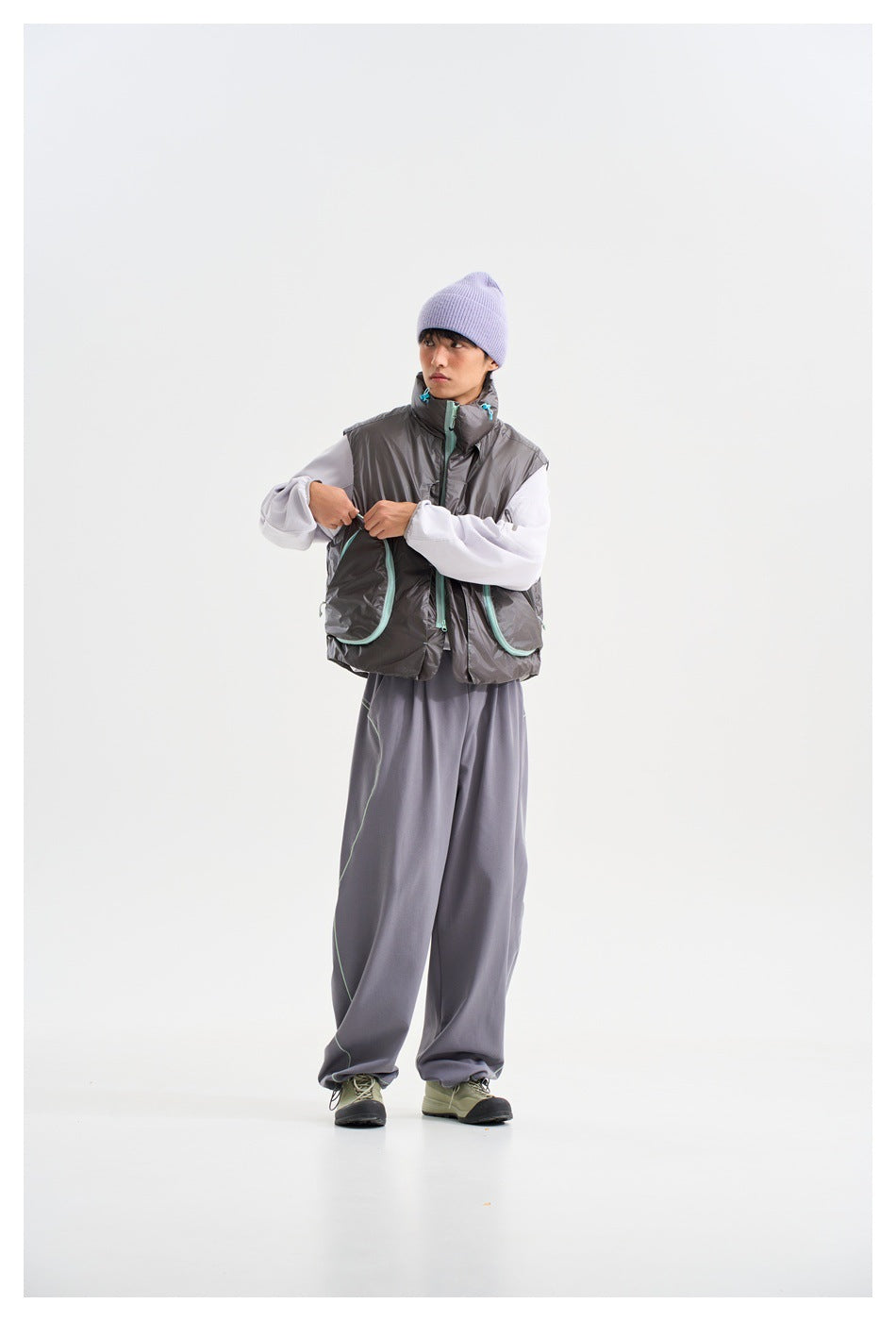 Model wearing a charcoal sleeveless vest with mint-trimmed pockets, white sleeves, gray trousers and a lavender beanie.