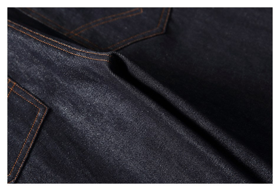 Close-up of dark denim folds and orange-stitched pocket seams.