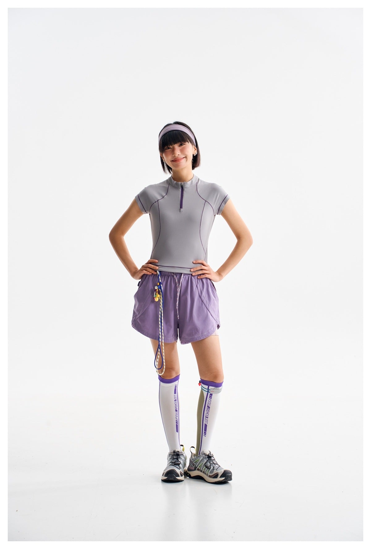 Model wearing a gray short-sleeve zip-neck top and lavender drawstring shorts with knee-high socks.