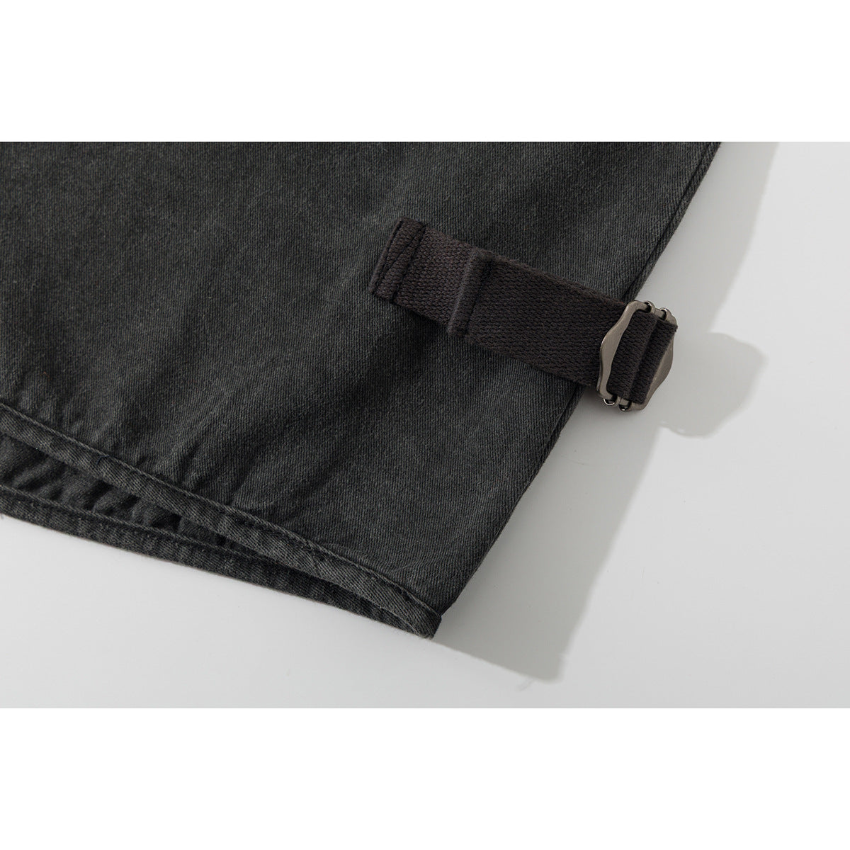 Close-up of a charcoal vest hem with an adjustable side strap and metal buckle.