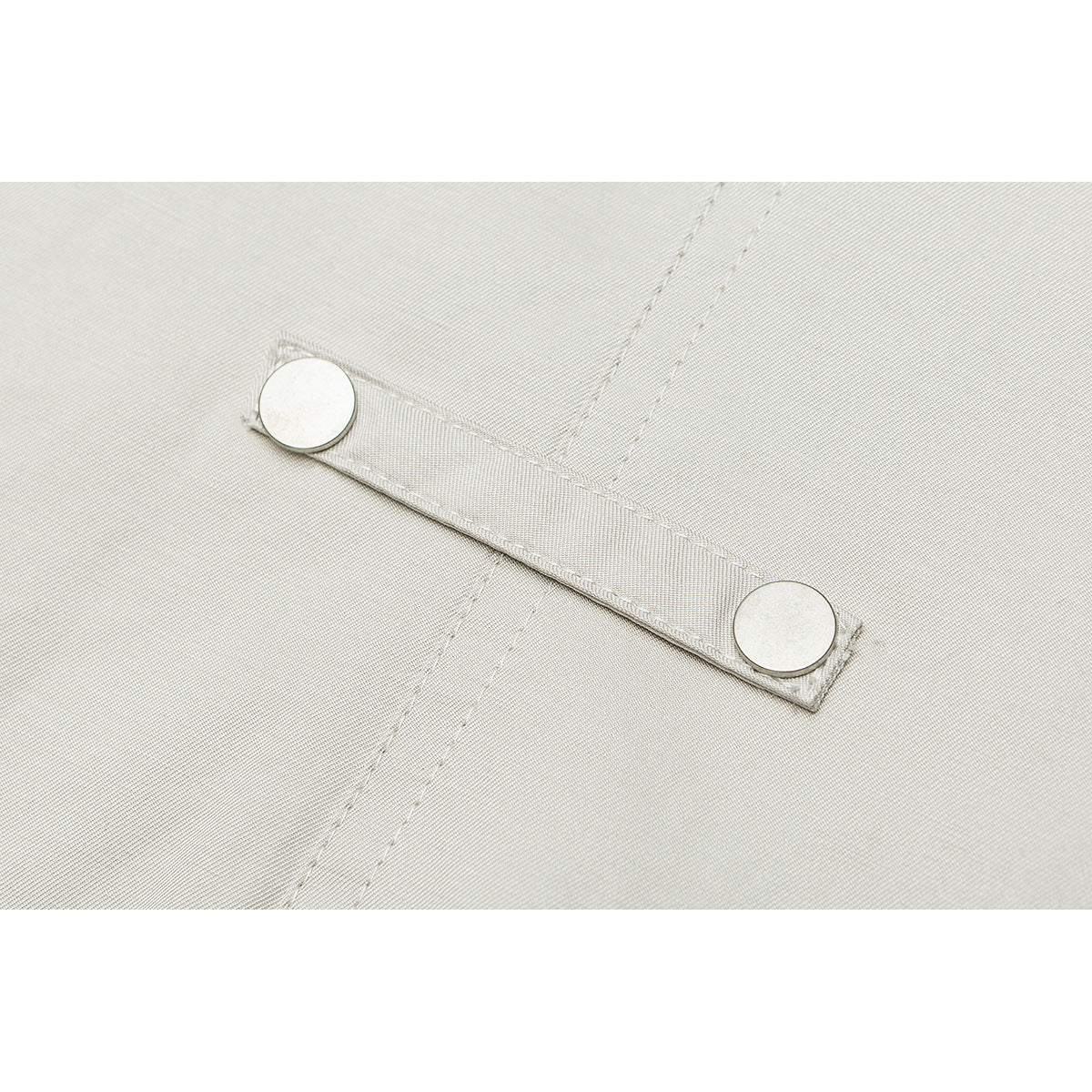 Close-up of a pale beige jacket strap with two round metal snaps and visible stitching.