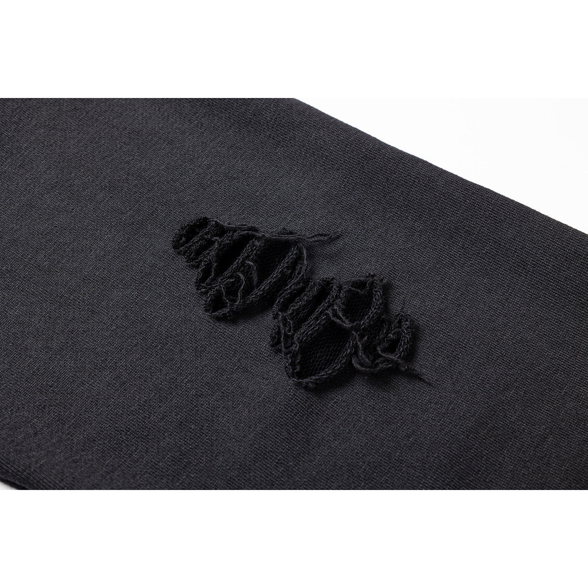 Close-up of a black distressed tear in dark fabric, showing loose frayed threads.