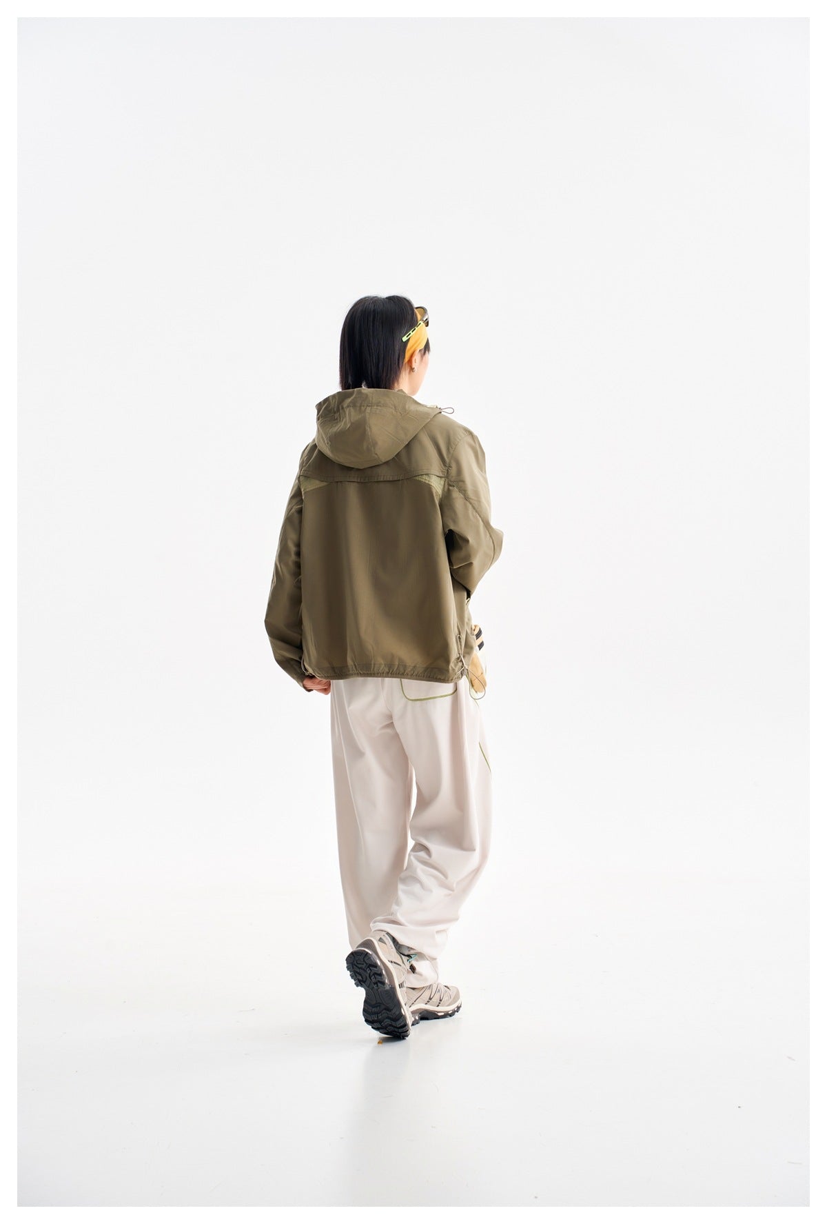 Model shown from behind wearing an olive hooded jacket with loose light pants.