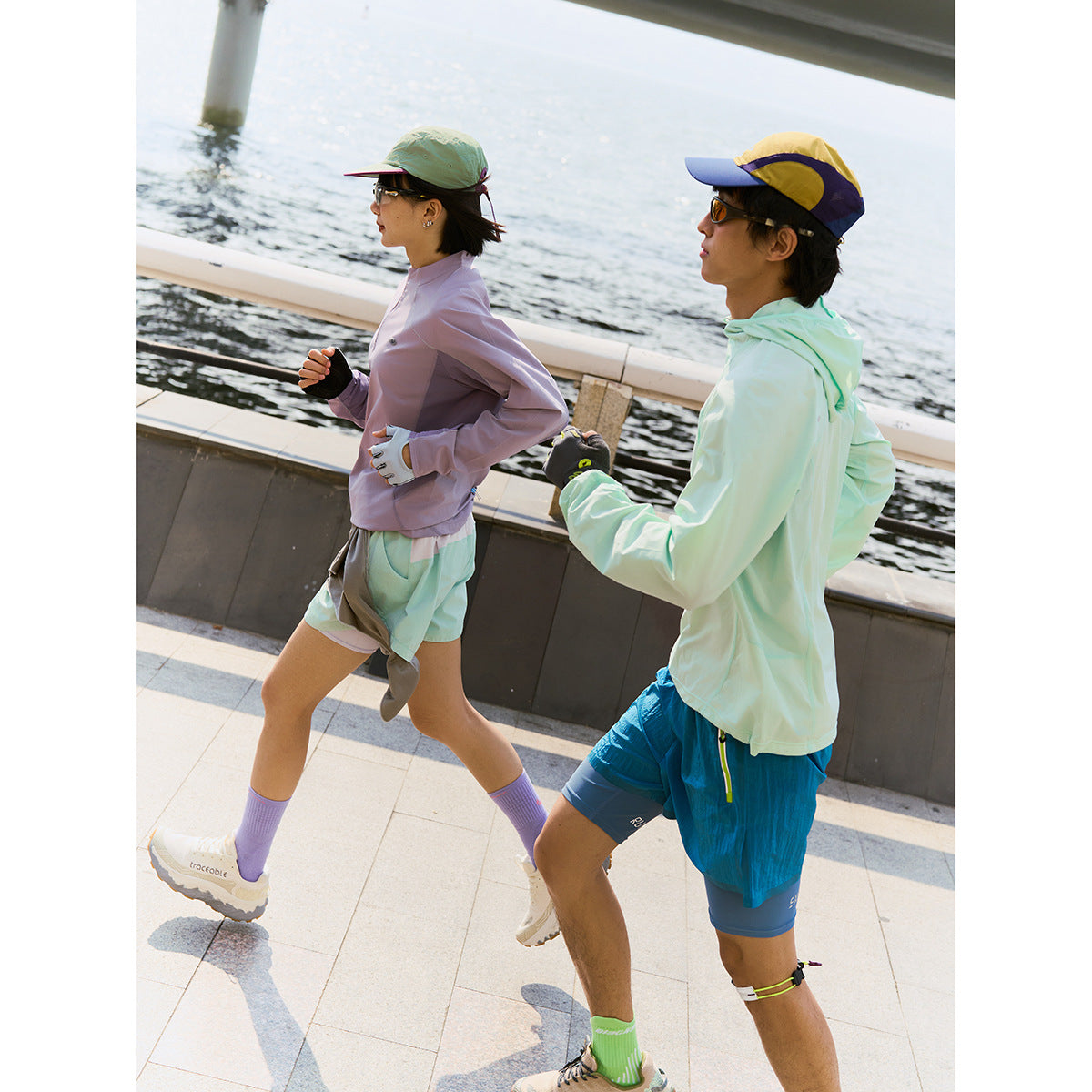 Two runners beside the water wearing lightweight sun-protective tops, shorts, caps, gloves, and running shoes.