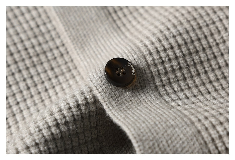 Macro view of a dark four-hole button on the light gray textured knit garment.