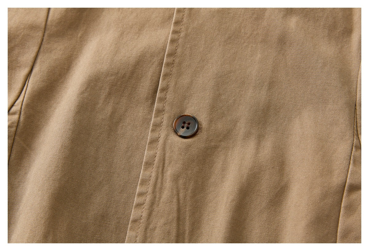 Close-up of a dark button and stitched placket on tan woven garment fabric.