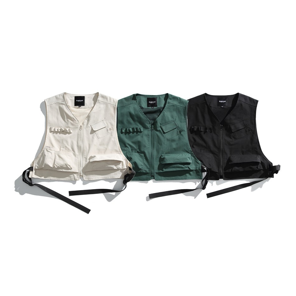 Three utility vests displayed together in cream, deep green, and black.