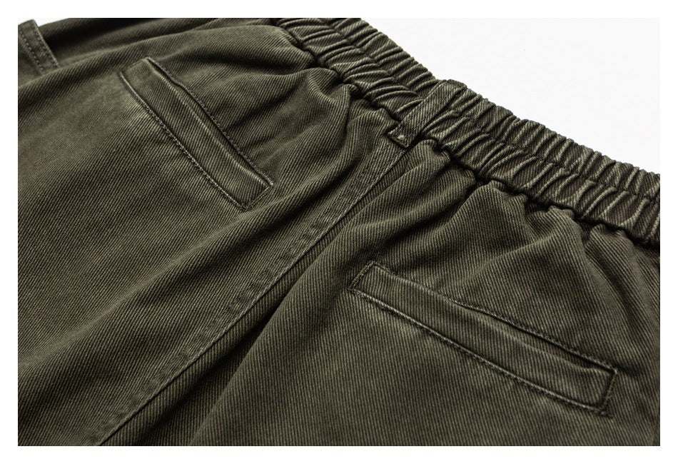 Close-up of dark olive trousers with an elastic waistband, belt loop and angled pocket openings.