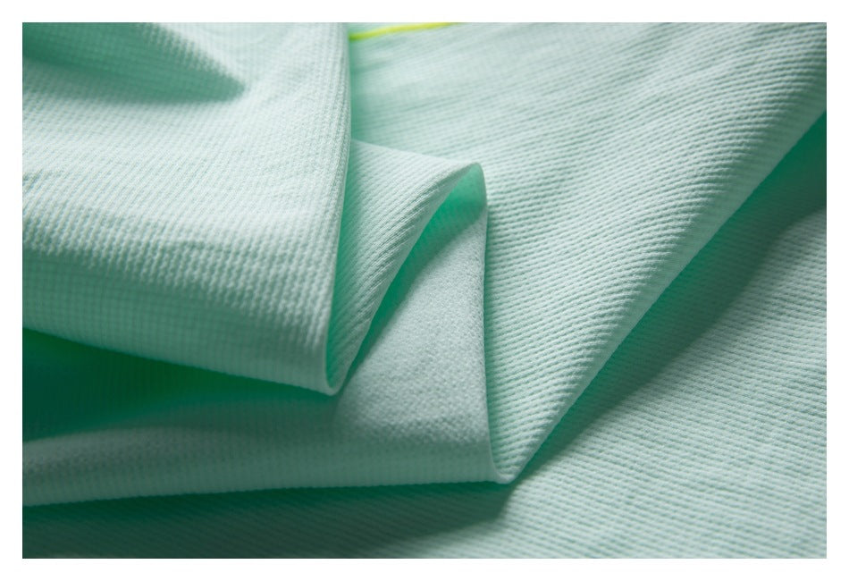 Close-up of folded pale mint textured garment fabric with a glimpse of lime piping.