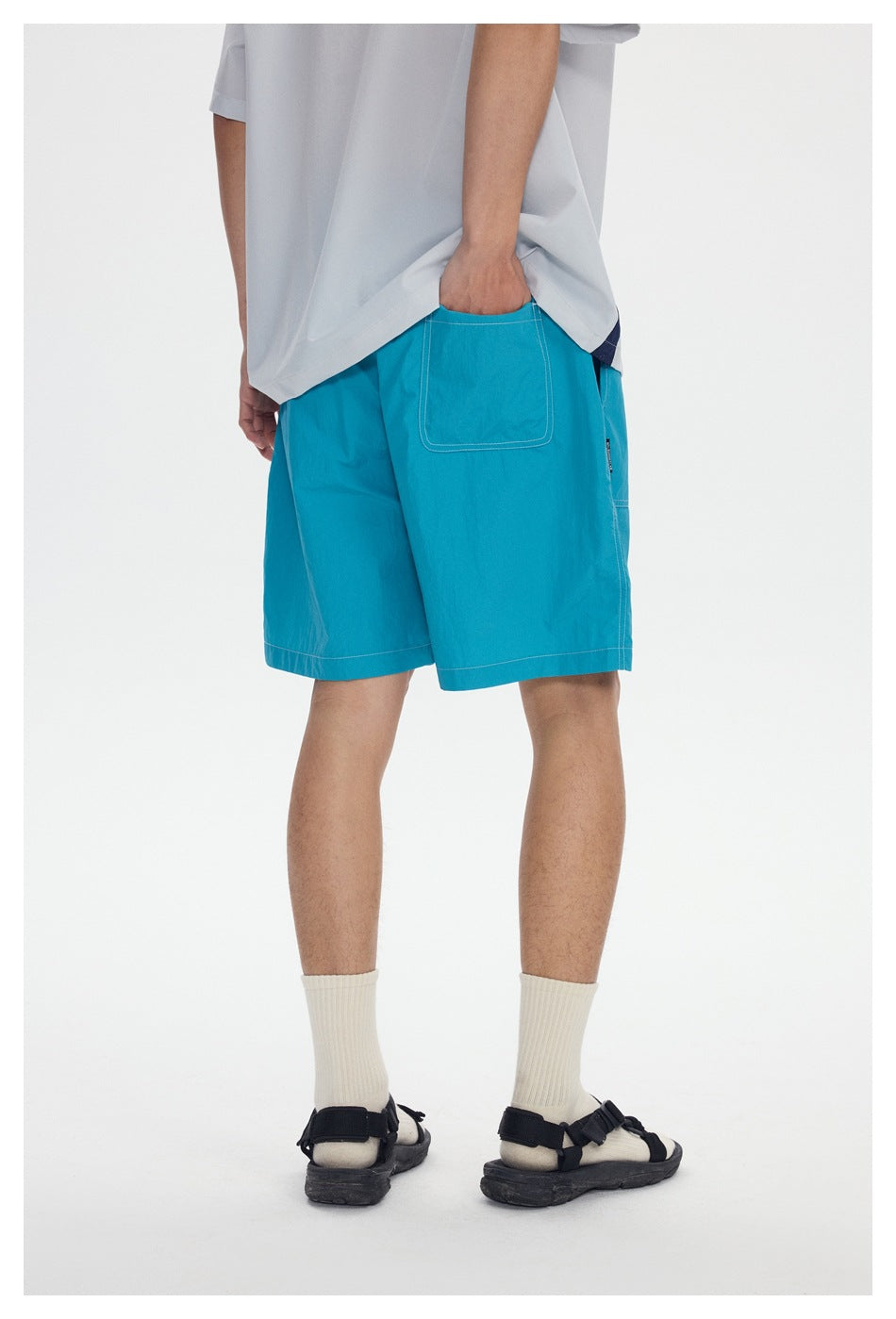 Rear view of a person wearing bright turquoise shorts with a back patch pocket and white contrast stitching.
