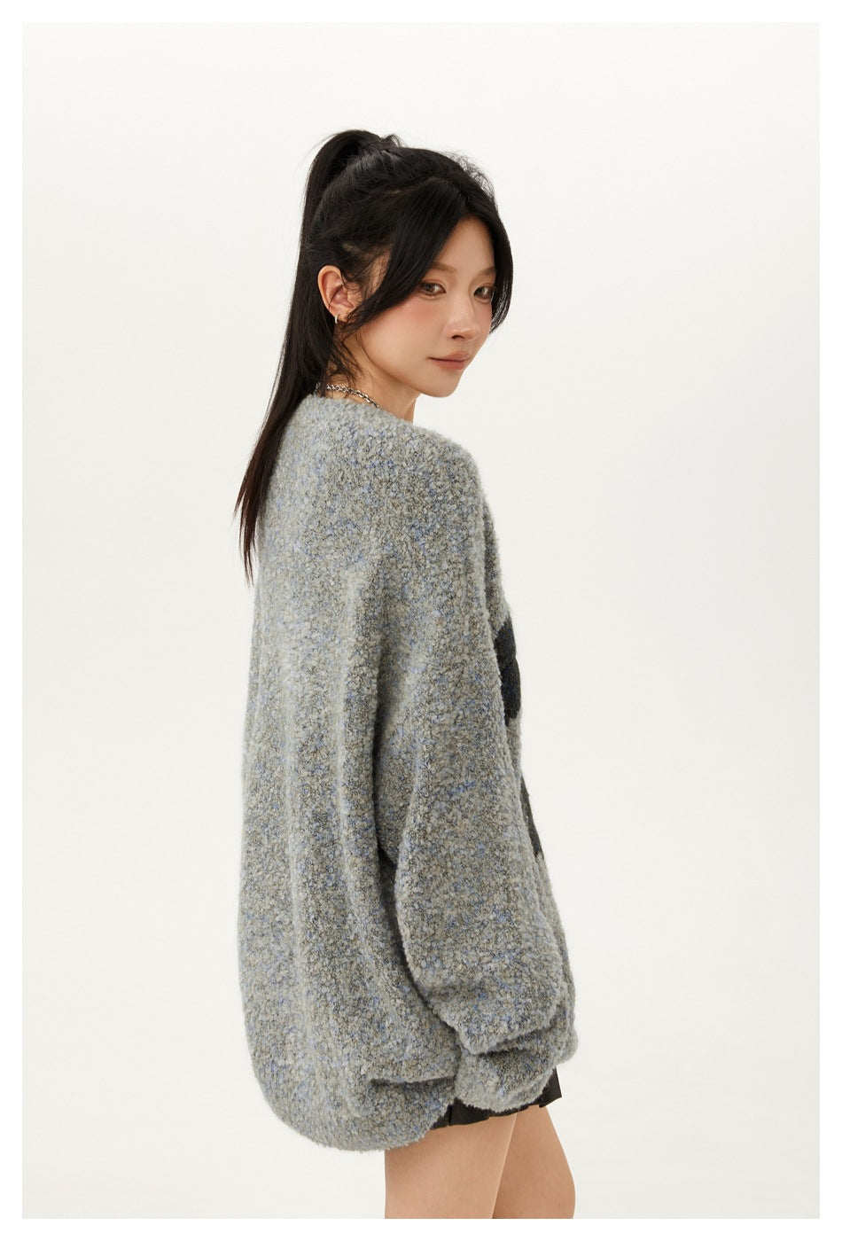 Model wearing an oversized blue-gray marled sweater with long sleeves, shown from the side and looking back.