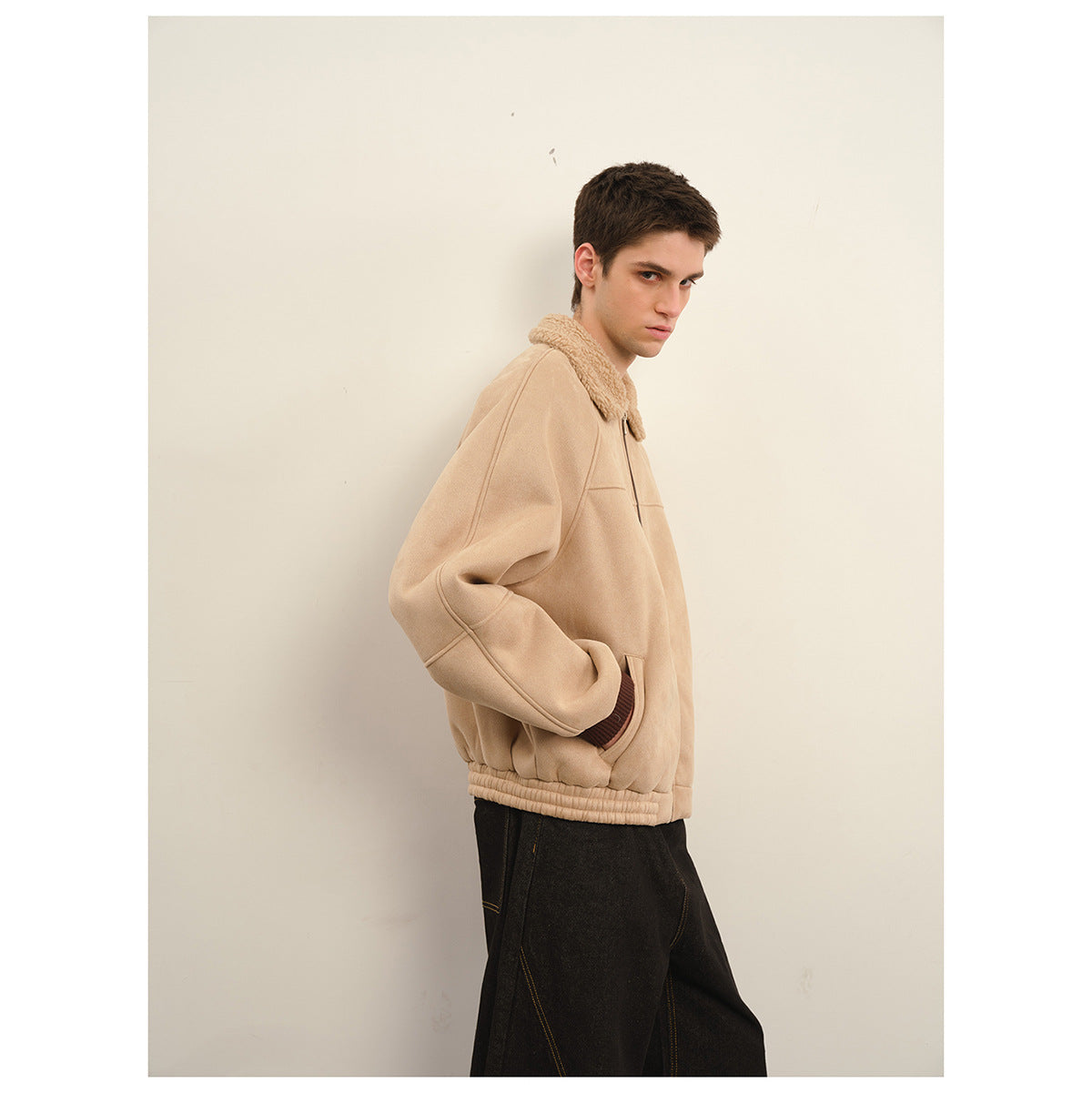 Side view of a model wearing a beige zip jacket with a plush collar and loose black trousers.