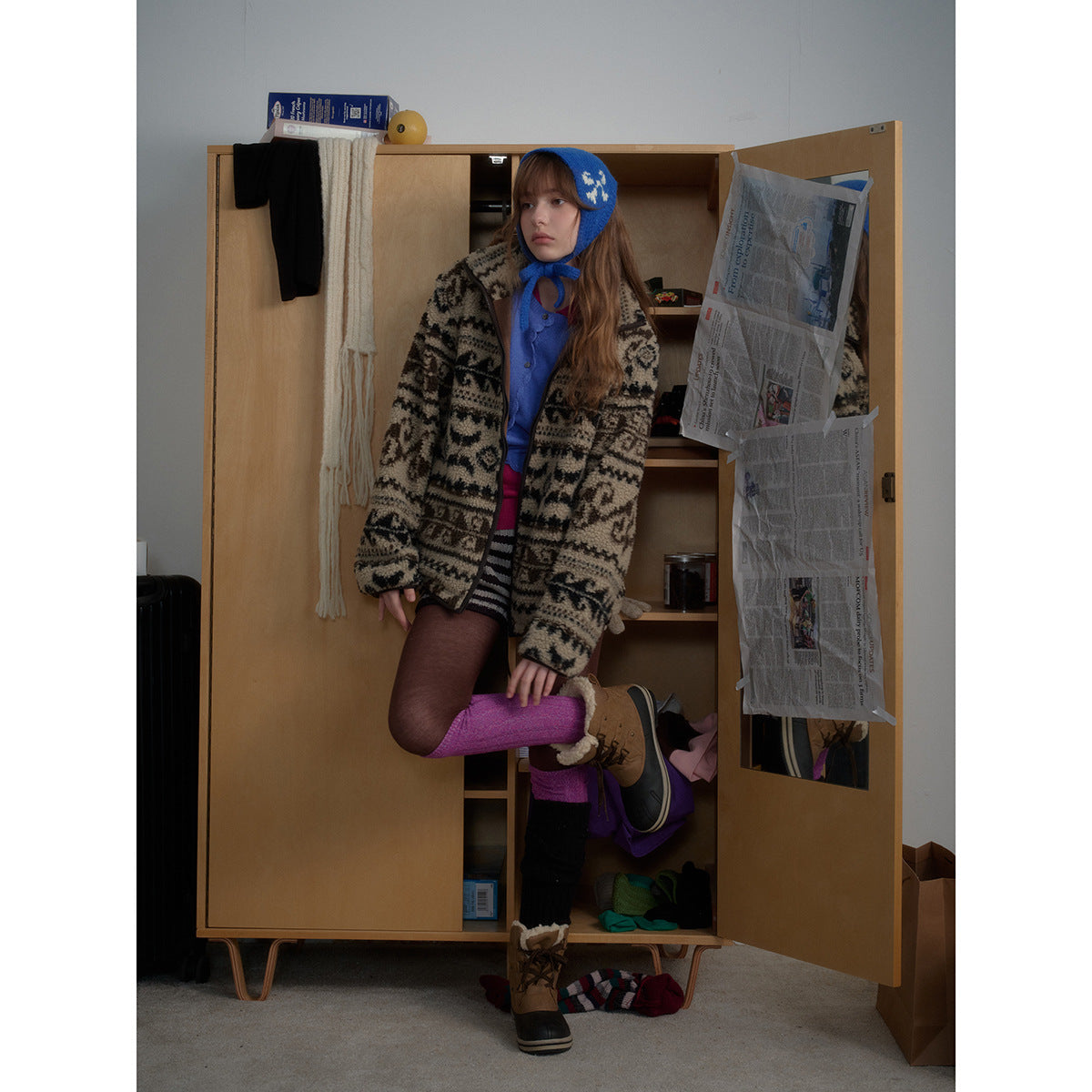 Model wearing a beige and black geometric zip cardigan over blue, with a matching blue knit bonnet.