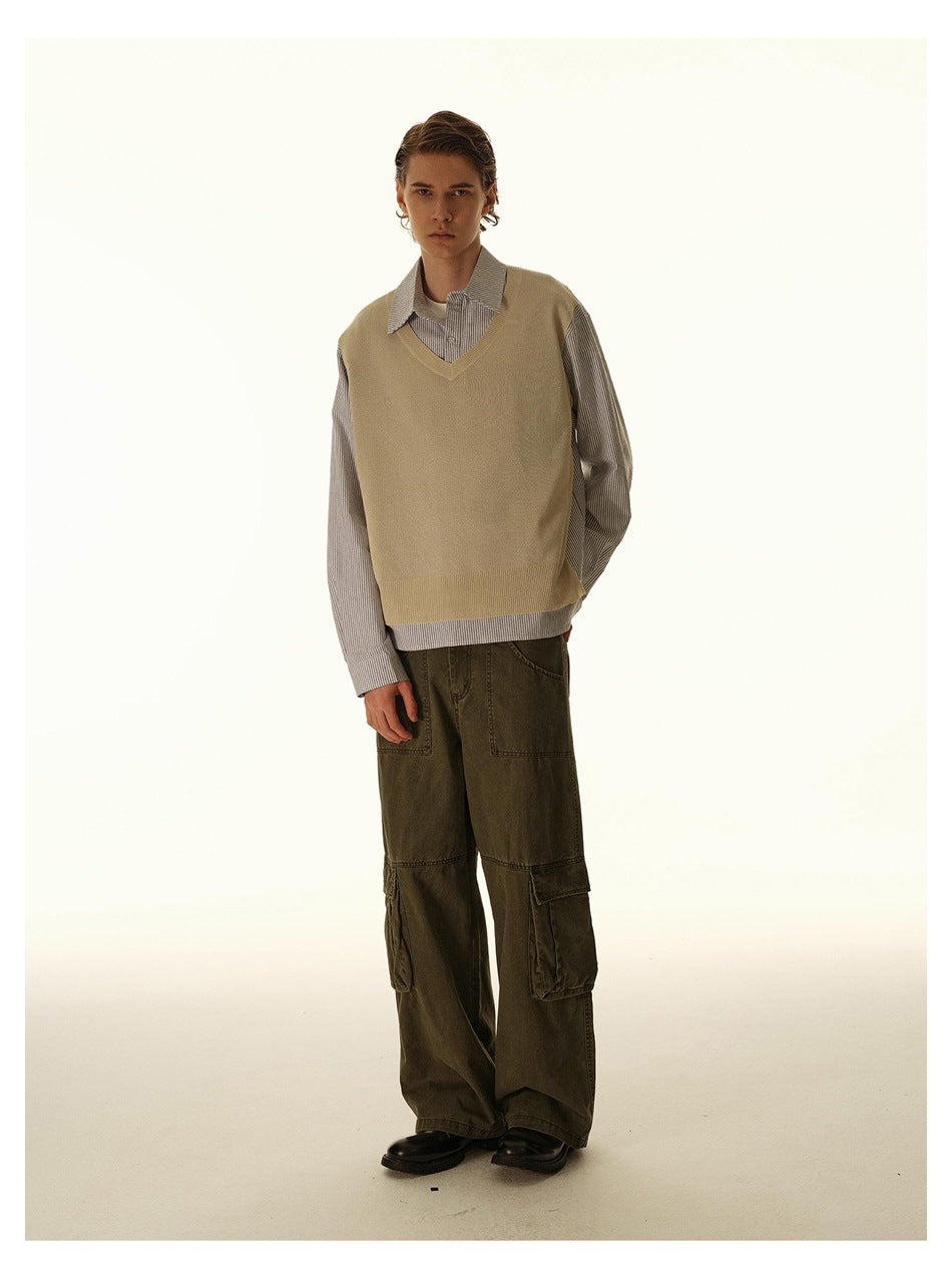 Male model in a beige V-neck vest layered over a striped shirt and olive cargo pants, standing at a slight angle.