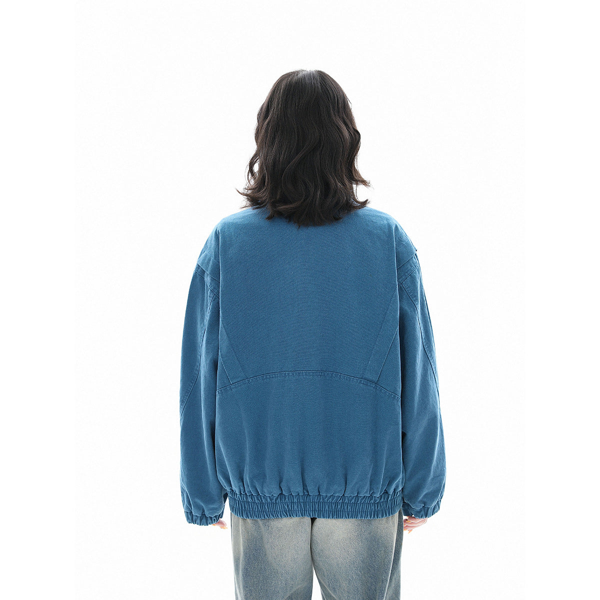 Back view of a model wearing a blue jacket with a curved back seam, long sleeves, and gathered hem.