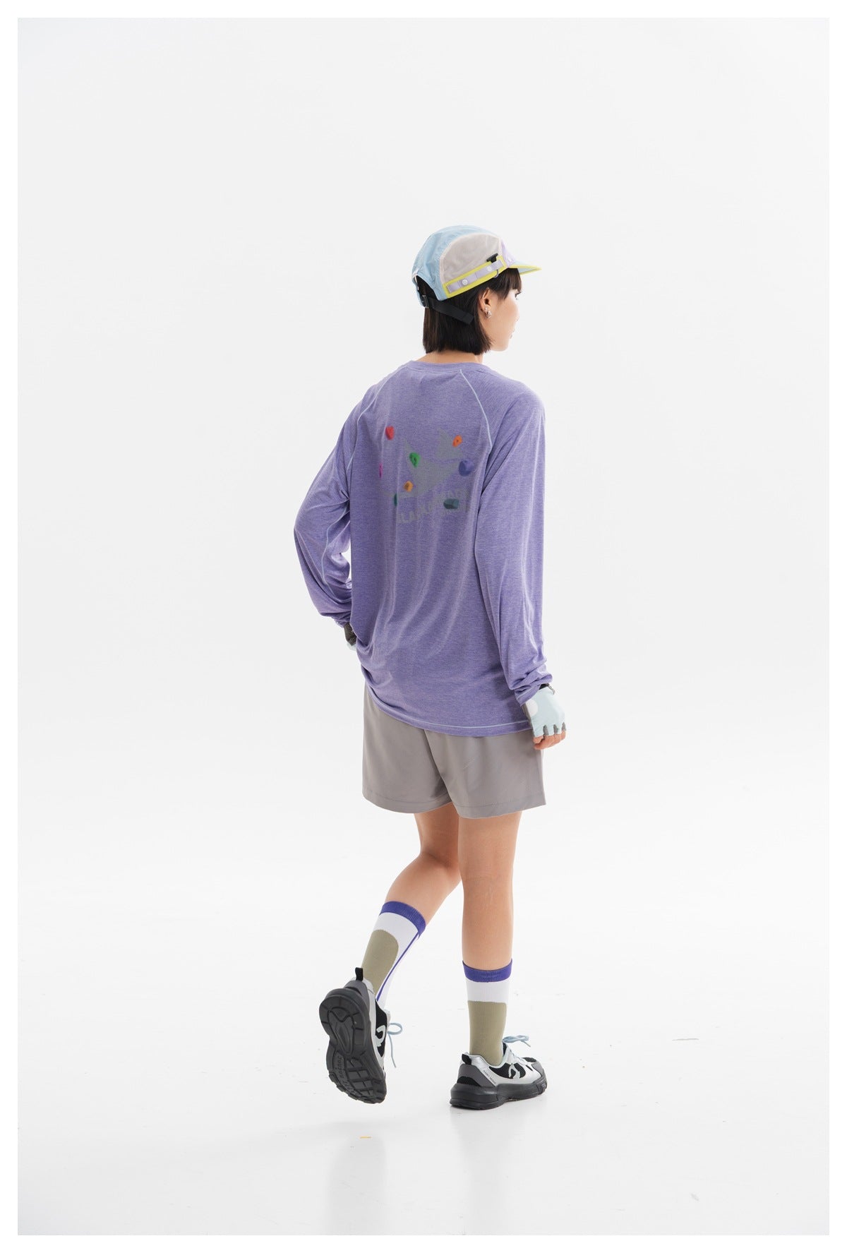 Rear view of a model in a lavender long-sleeve shirt with a colorful back graphic and gray shorts.