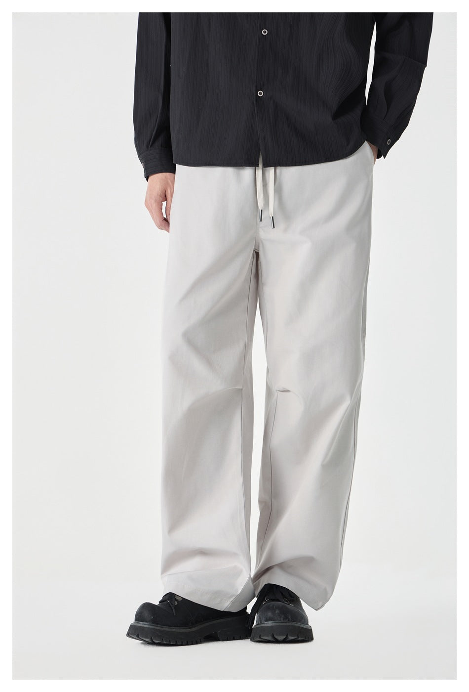 Model wearing beige wide-leg drawstring pants with a black striped shirt and chunky black shoes, front view