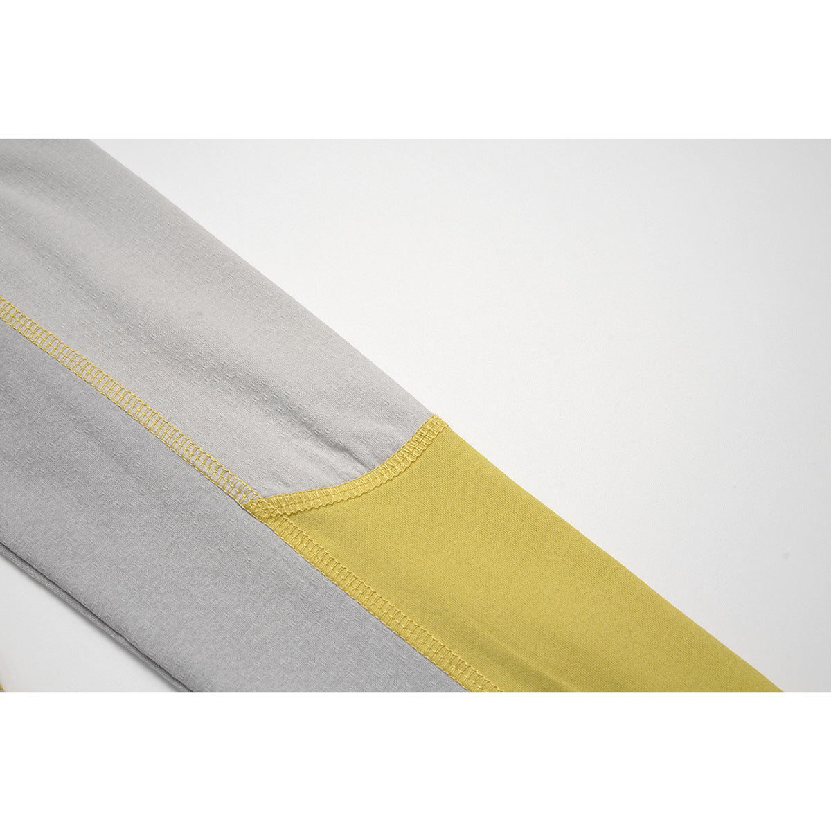 Close-up of a light gray sleeve with a mustard-yellow color-block panel and contrast stitching.