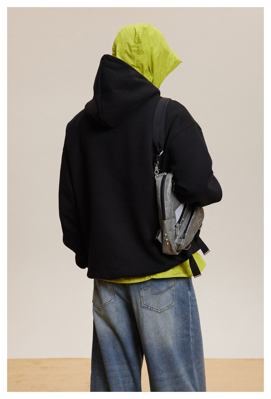 Back view of a person wearing a plain black hoodie over a neon yellow hooded layer and blue jeans.