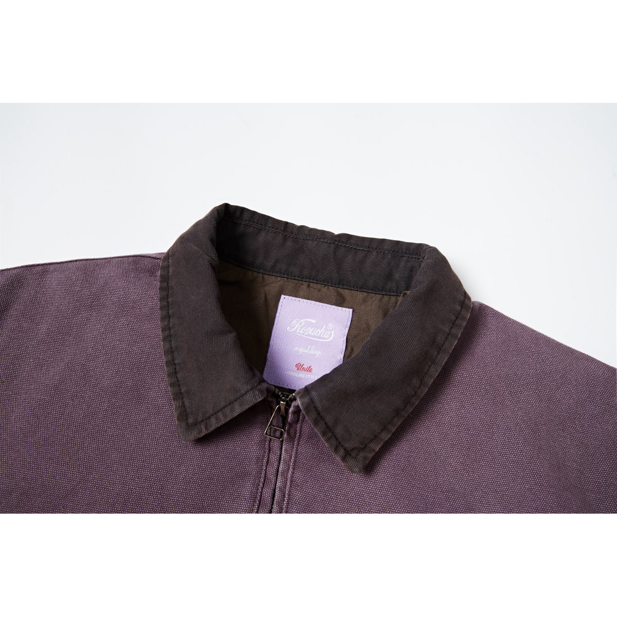 Close-up of a plum jacket's dark collar, front zipper, and sewn inner neck label.