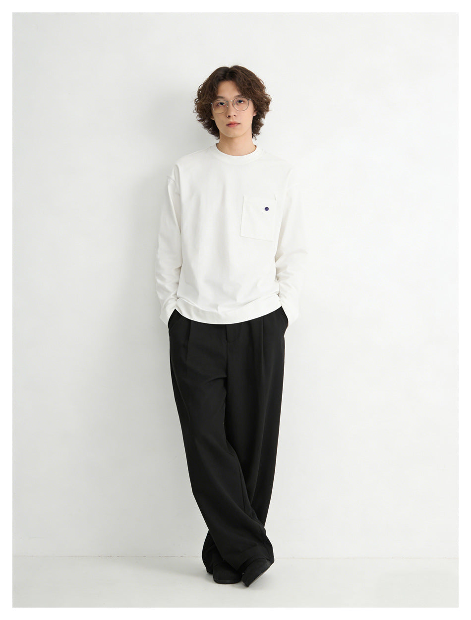 Front view of a model wearing a white long-sleeve crewneck top with a chest pocket and black trousers.