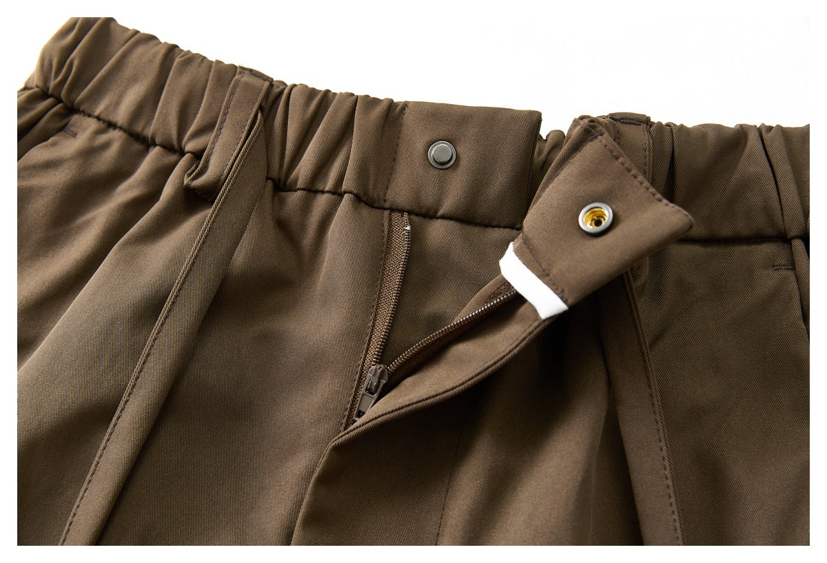 Close-up of brown trousers with an elasticated waistband, snap closure and partially open zip fly.