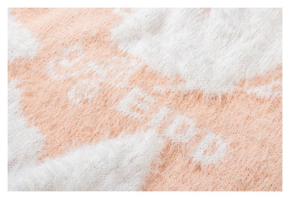 Close-up of the sweater's fuzzy knit texture and white pattern against blush pink.