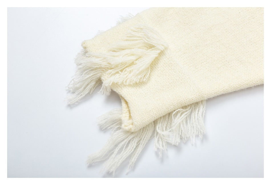 Close-up of cream fringe at the cuff of a cream knit sweater.