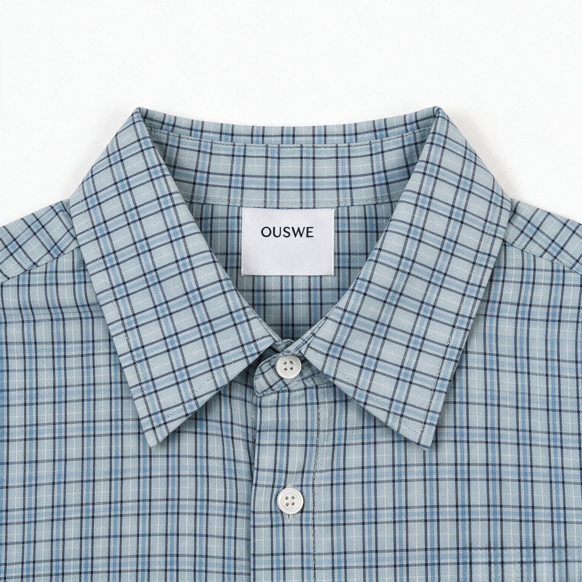 Close-up of a pale blue plaid shirt collar, white buttons, and a sewn-in OUSWE label.