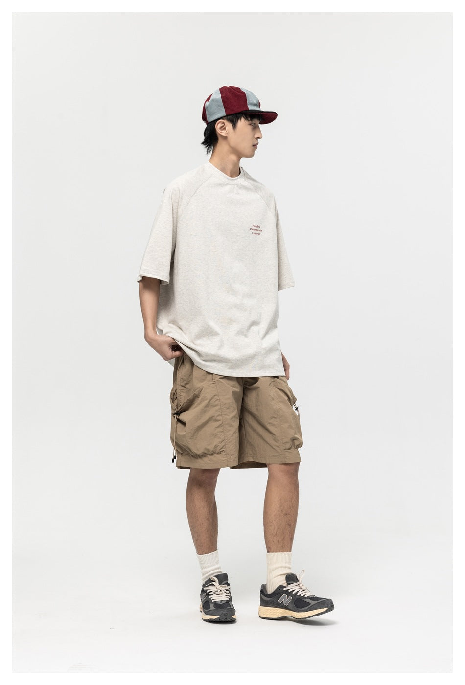 Model wearing light gray raglan-sleeve T-shirt with khaki cargo shorts, cap and sneakers, side view