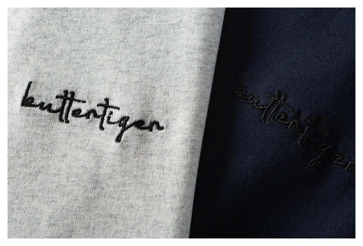 Close-up of black script embroidery on heather-gray and navy shirt fabric.