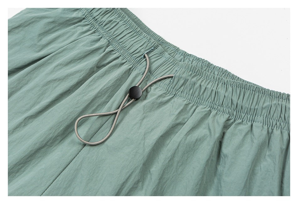 Close-up of sage green shorts with a gathered elastic waistband and gray drawcord with a black toggle.