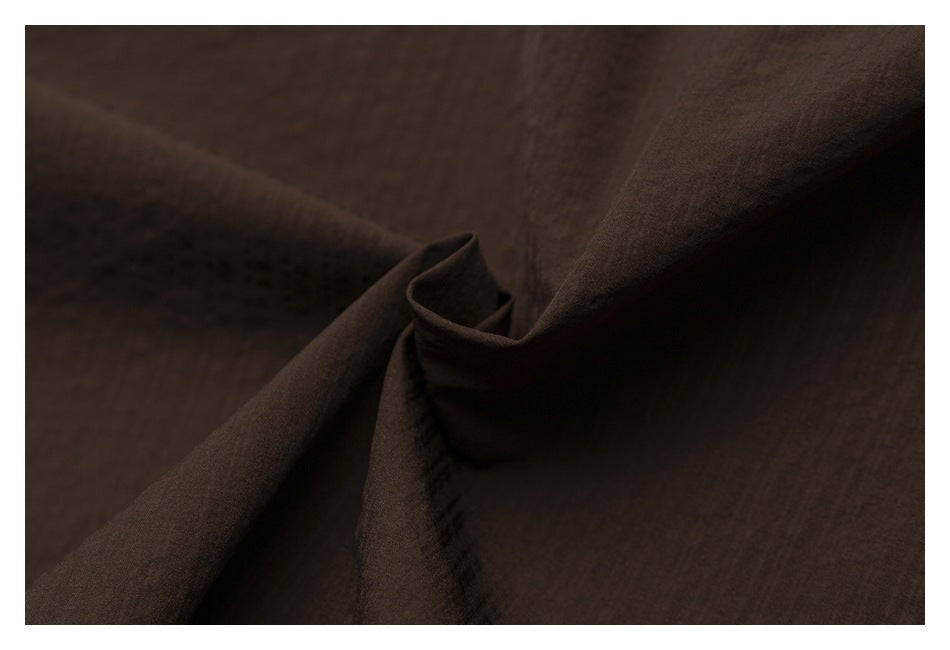 Dark brown fabric gathered into folds, showing its surface texture.