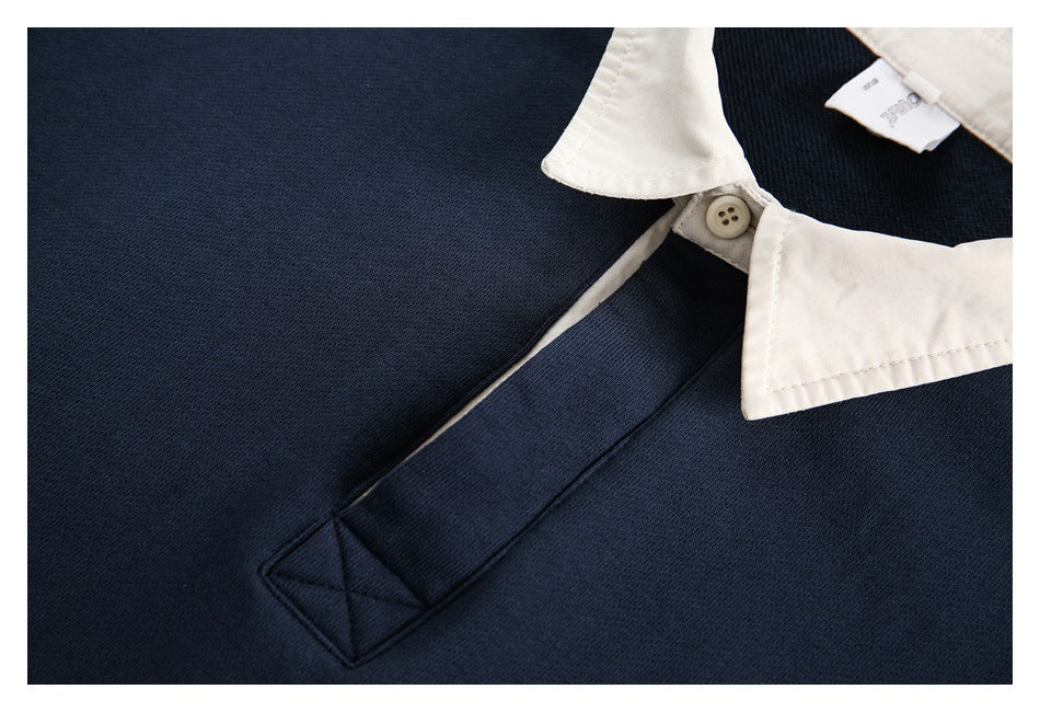 Close-up of the cream collar and button above the navy sweatshirt's stitched front placket.