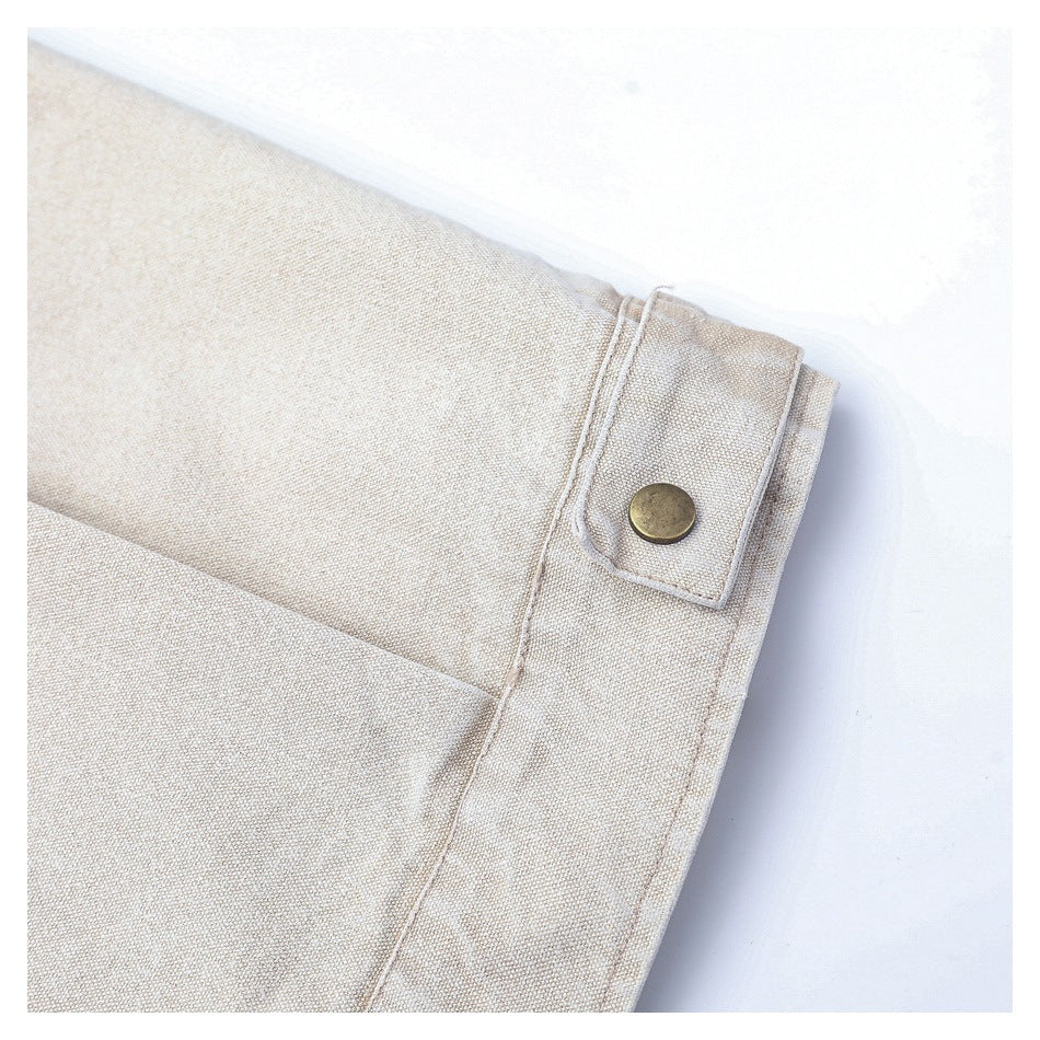 Close-up of a beige woven garment cuff with a stitched tab and round brass-tone button.