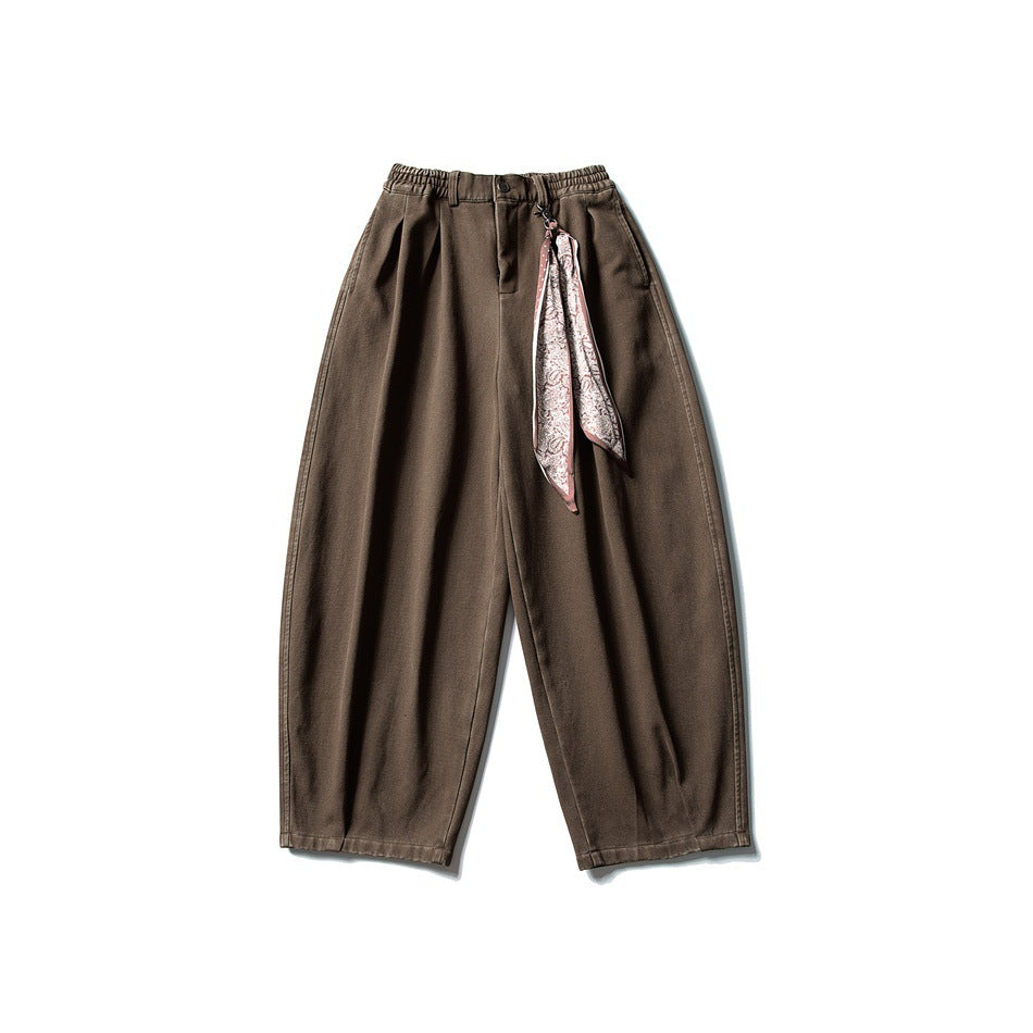 Front view of relaxed brown trousers with an elastic waist and a pink paisley scarf tied at the waistband.