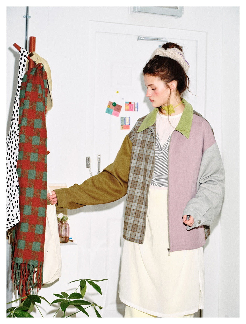 Model wearing color-block zip jacket with green collar over striped top and cream dress, reaching toward a coat rack