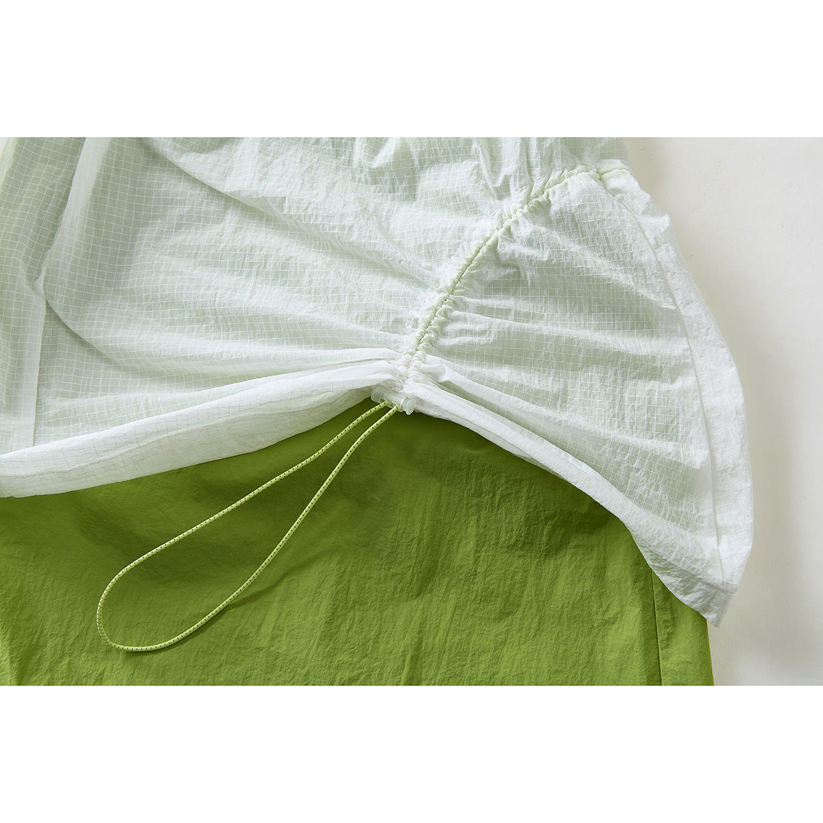 Close-up of an adjustable side drawcord gathering the pale grid-patterned skirt over a green underlayer.