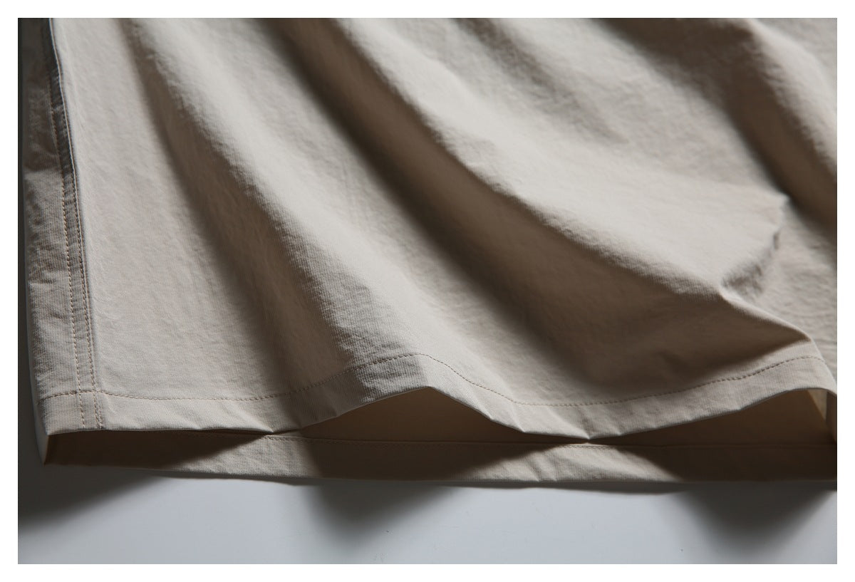 Close-up of the double-stitched hem and side seam of a light taupe shirt.