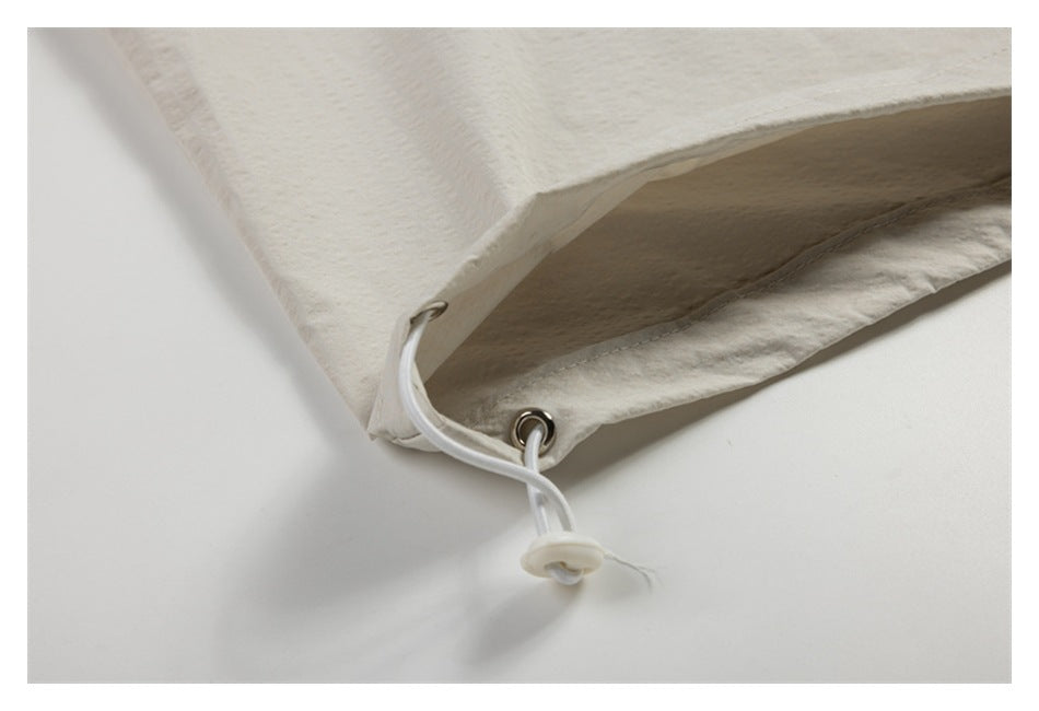 Close-up of the off-white garment's hem with metal eyelets and a white drawcord toggle.