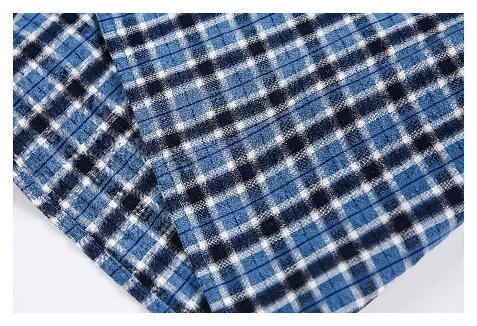 Close-up of blue, navy and white plaid shirt fabric with a stitched edge and overlapping folds.
