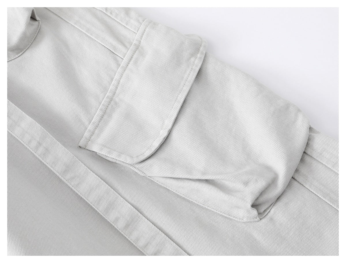 Close-up of a flap pocket on light gray trousers, showing its stitching and diagonal twill texture.