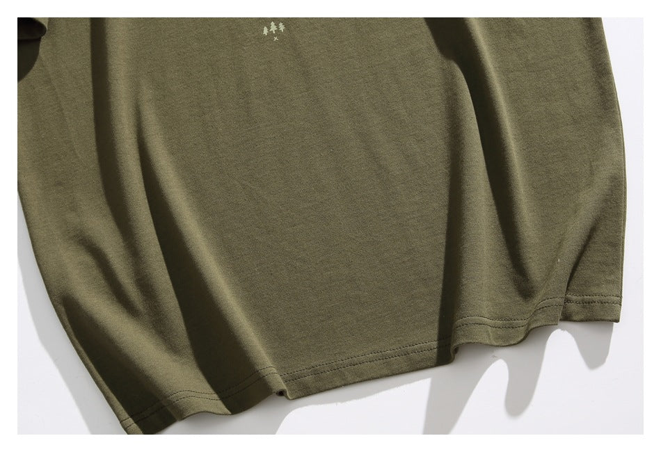Close-up of an olive green T-shirt hem with double stitching and a small pale tree motif.