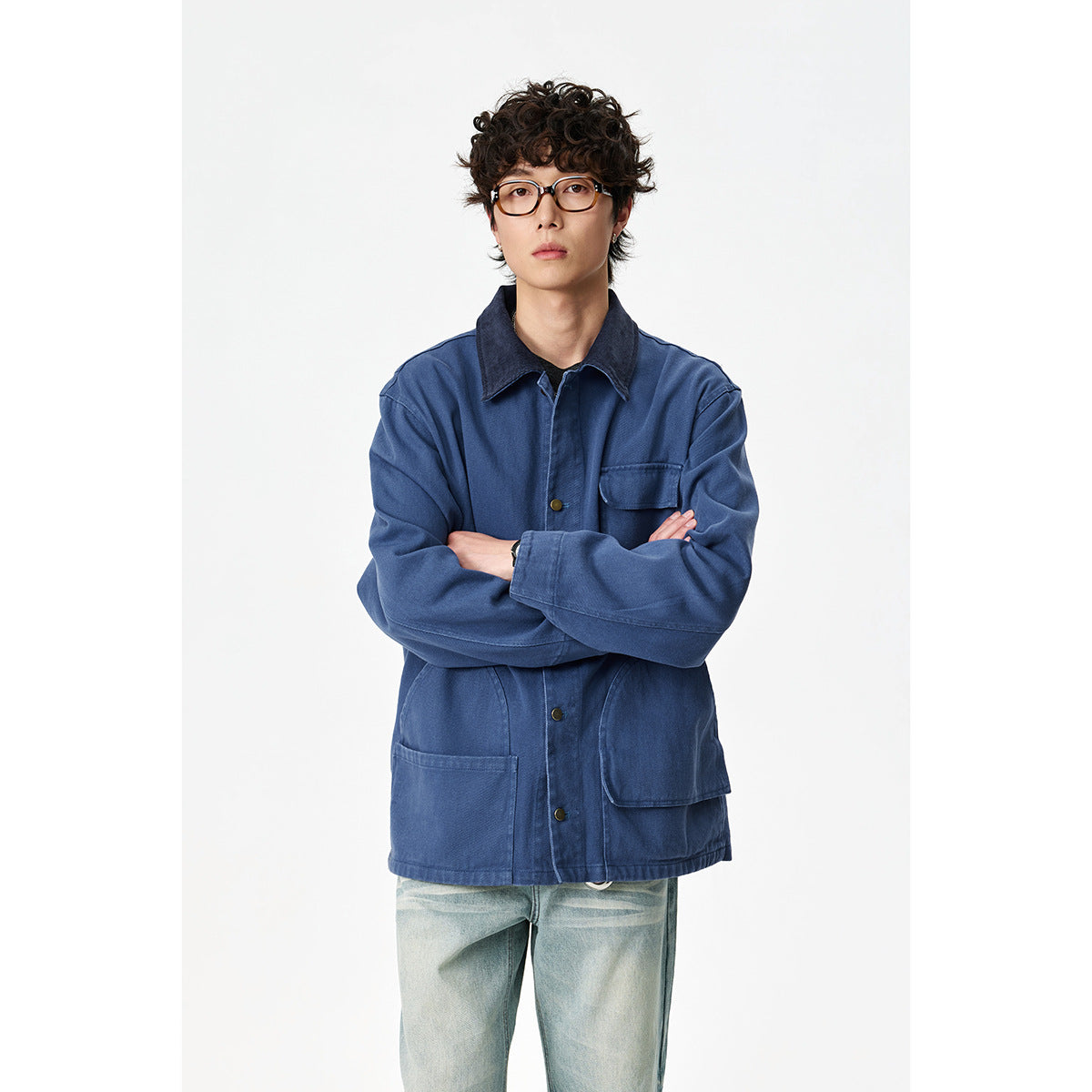 Front view of a model in a blue work jacket with a dark collar, brass-tone buttons and roomy patch pockets.