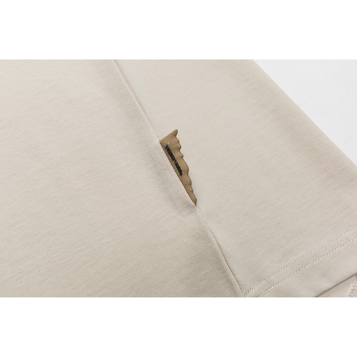 Close-up of a beige garment seam with a small tan fabric tab.